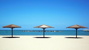 Tre ombrelloni sulla spiaggia sabbiosa, con cielo azzurro limpido e mare calmo.