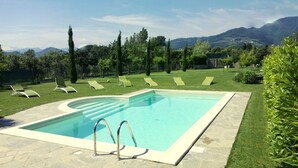 Una piscina rettangolare con bordo in pietra, circondata da un prato curato e diverse poltrone prendisole.