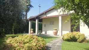 Un edificio con un portico coperto, grandi piante in vaso e un prato curato.