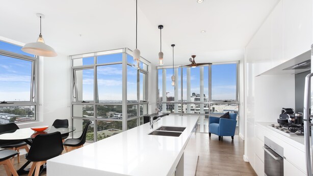 A modern kitchen with a large island, white cabinetry, and a view of the city. - As the Sun Sets (Zetland)