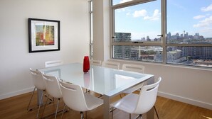 A modern meeting room with a glass table, white chairs, a framed artwork on the wall, and a large window with a city view. - Moore to See (Zetland)