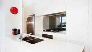 A modern kitchen with a stainless steel refrigerator, a built-in stove, and a red clock on the wall. - Moore to See (Zetland)