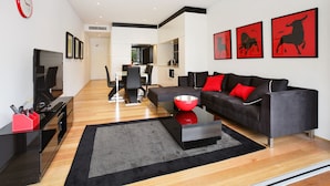 A modern living room with a black sofa, red cushions, a flat-screen TV, and a dining area in the background. - New York on Riley (Darlinghurst)