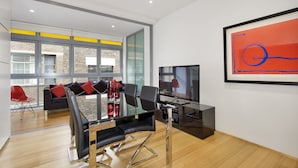 A modern living room with a glass table, black chairs, a sofa with red cushions, and a large window with a view of a brick building. - Little New York on Riley (Darlinghurst)