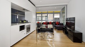 A modern kitchen with built-in appliances, a dining area with a glass table and chairs, and a living area with a sofa and TV. - Little New York on Riley (Darlinghurst)