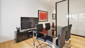 A modern living room with a flat-screen TV, a glass coffee table, and black leather chairs. - Little New York on Riley (Darlinghurst)