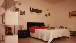 A bedroom with a bed, a nightstand, a TV, and a shelf with books and decorative items. - Apartment in Countryside Villa With Pool Within the Se Sicilian Barocco Area (Ragusa)