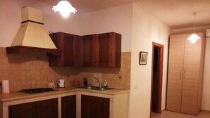 A compact kitchen with a gas stove, a sink, and wooden cabinets. There is a ceiling light fixture above the stove and a door leading to another room. - Apartment in Countryside Villa With Pool Within the Se Sicilian Barocco Area (Ragusa)