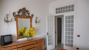 A bedroom with a wooden dresser, a mirror, a television, and a red bedspread. - Solaria 1 and 2 - Ospedaletti Ligure - Lungomare C Colombo Nrfloor (Ospedaletti)