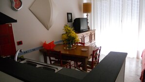 A kitchen with a dining table, chairs, a vase with flowers, a clock, and a television on a cabinet. - Solaria 1 and 2 - Ospedaletti Ligure - Lungomare C Colombo Nrfloor (Ospedaletti)