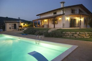 Uma casa de dois andares com piscina, área de estar externa e muro de pedra.
