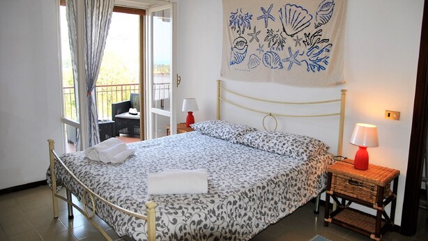 A bedroom with a bed, two bedside tables with lamps, a wall tapestry, and a balcony with a chair. - Villa Lina for 7 Persons Near the Beach (Fondi)