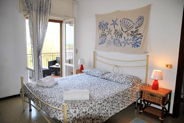 Une chambre à coucher avec un lit, deux tables de chevet avec des lampes, une tapisserie murale et un balcon avec une chaise.