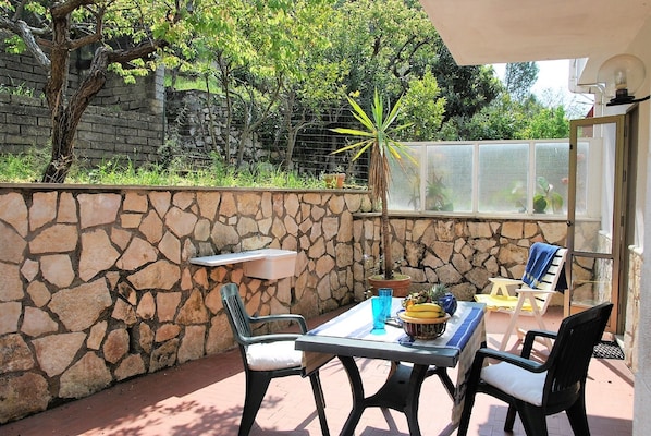 Une terrasse extérieure avec un mur en pierre, une table avec des chaises, un pot de fleurs et une vue sur la végétation environnante.