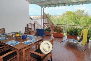 Une terrasse avec une table dressée pour le repas, des chaises, un chapeau et des plantes en pot.