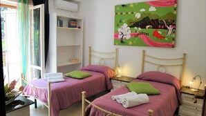 A room with two beds, a wall-mounted air conditioner, a shelf with books, and a colorful painting. - Villa Lina for 7 Persons Near the Beach (Fondi)