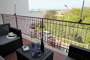 Un balcon avec des meubles en osier, un chapeau, un livre et une bouteille.
