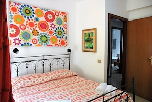 Un lit recouvert d’une couvre-lit à motifs floraux, une œuvre d’art colorée accrochée au mur et un tableau encadré.