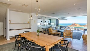 A modern kitchen with a central island, dining area with a wooden table and chairs, and a view of the ocean. - Zimbali by Euphoric, Zimbali Coastal Resort, Ballito (Ballito)
