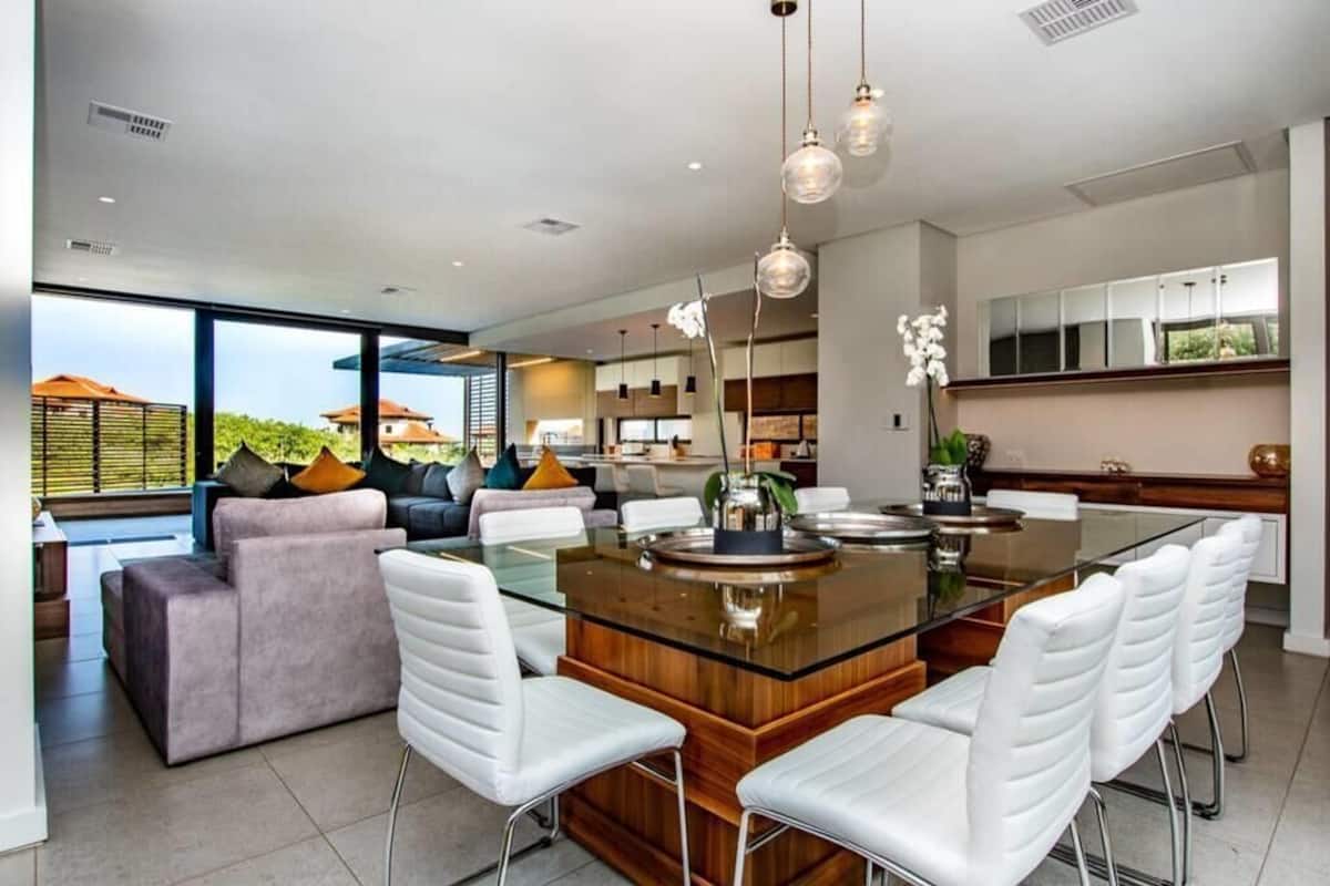 A modern kitchen with a central island, white bar stools, and pendant lighting.