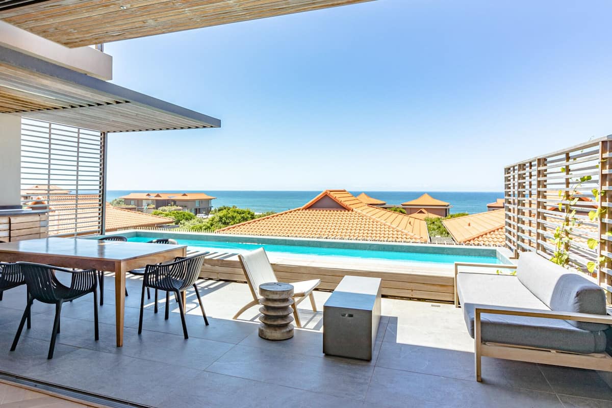 A terrace with a pool, outdoor seating, and a view of the sea.