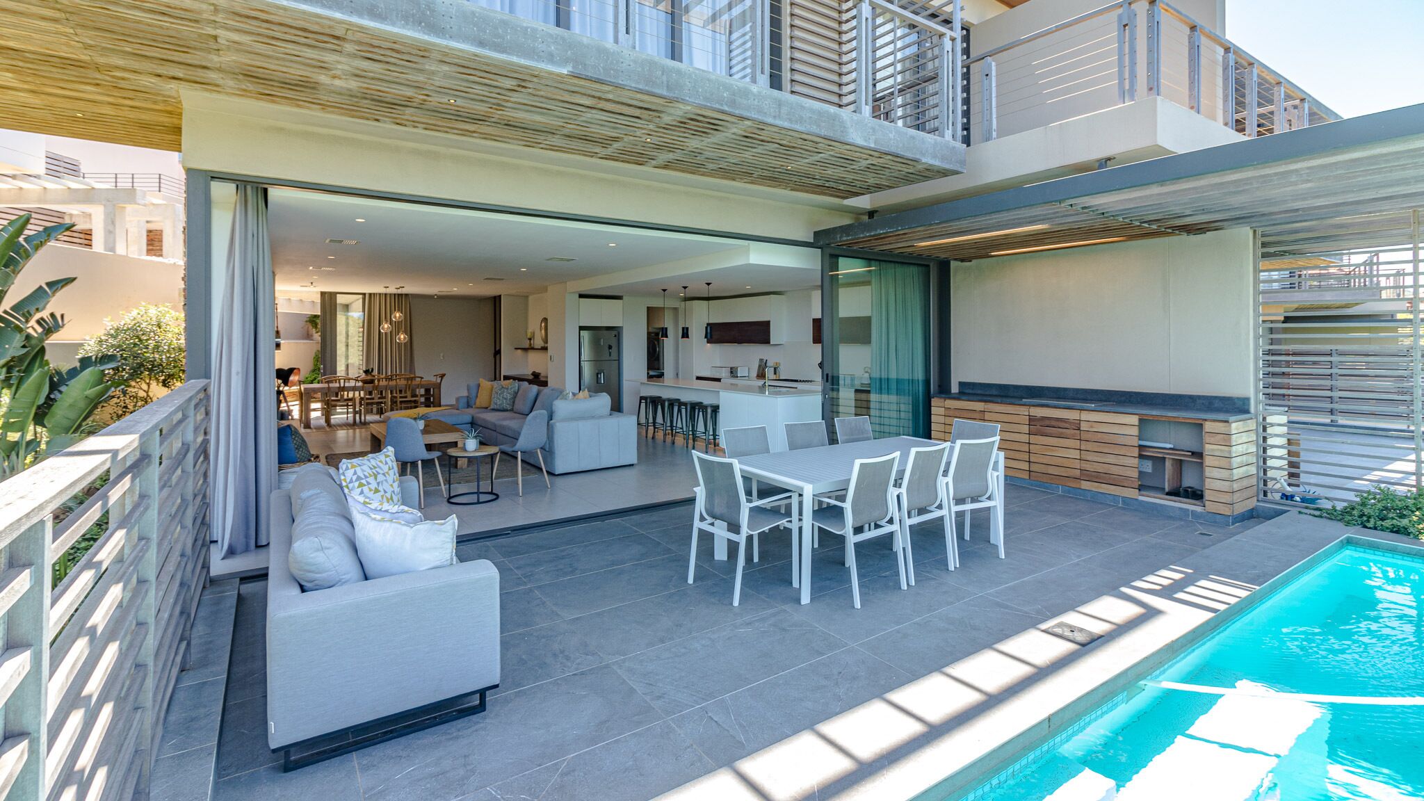 A modern outdoor living area with a pool, a dining set, and a kitchen visible through an open space.