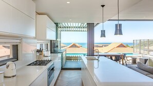 A modern kitchen with a view of the sea, a dining area with outdoor seating, and a large window overlooking the ocean. - Zimbali by Euphoric, Zimbali Coastal Resort, Ballito (Ballito)