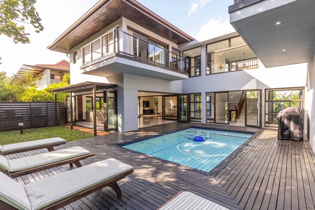 A modern two-story house with a swimming pool, outdoor seating, and large windows.