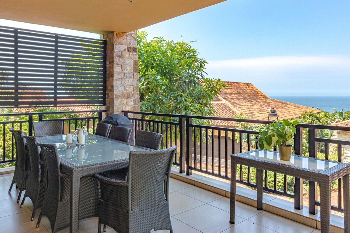 A balcony with wicker furniture, a glass table, and a view of the sea.