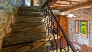 Una escalera con paredes de piedra y vigas de madera, que conduce a una habitación con ventana y vistas al verdor.