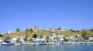 A coastal town with a historic tower, boats docked along the waterfront, and residential buildings.