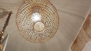 Une pièce avec une rambarde blanche, un lit recouvert d’une couvre-lit à motifs et un luminaire suspendu en forme de suspension tissée.