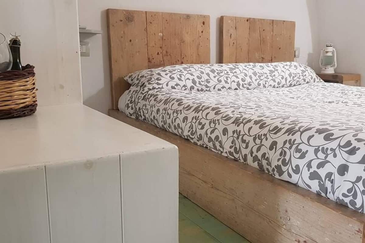 A bedroom with a wooden bed frame, a white bedside table, a lamp, and a wicker basket.