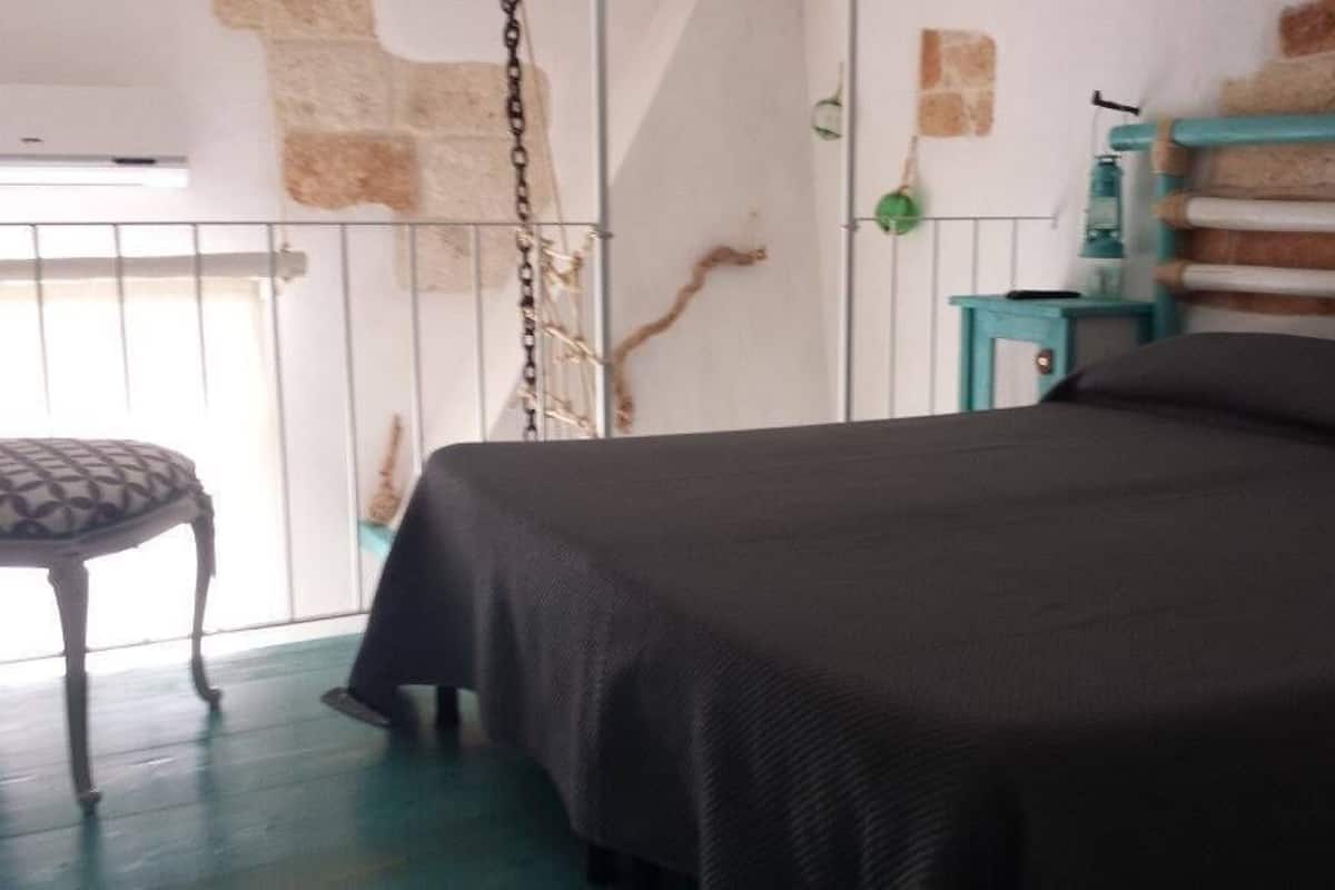 A bedroom with a bed, a chair, and a small table with a lamp.