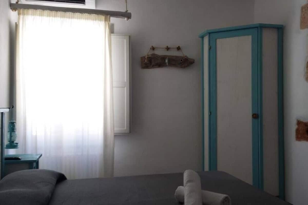 A bedroom with a bed, a window with curtains, a wall-mounted TV, and a blue door.