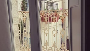 Une vue à travers une porte vitrée, ornée d’une grille en métal décorative, qui donne sur un espace extérieur avec un mur blanc et un pot de fleurs.