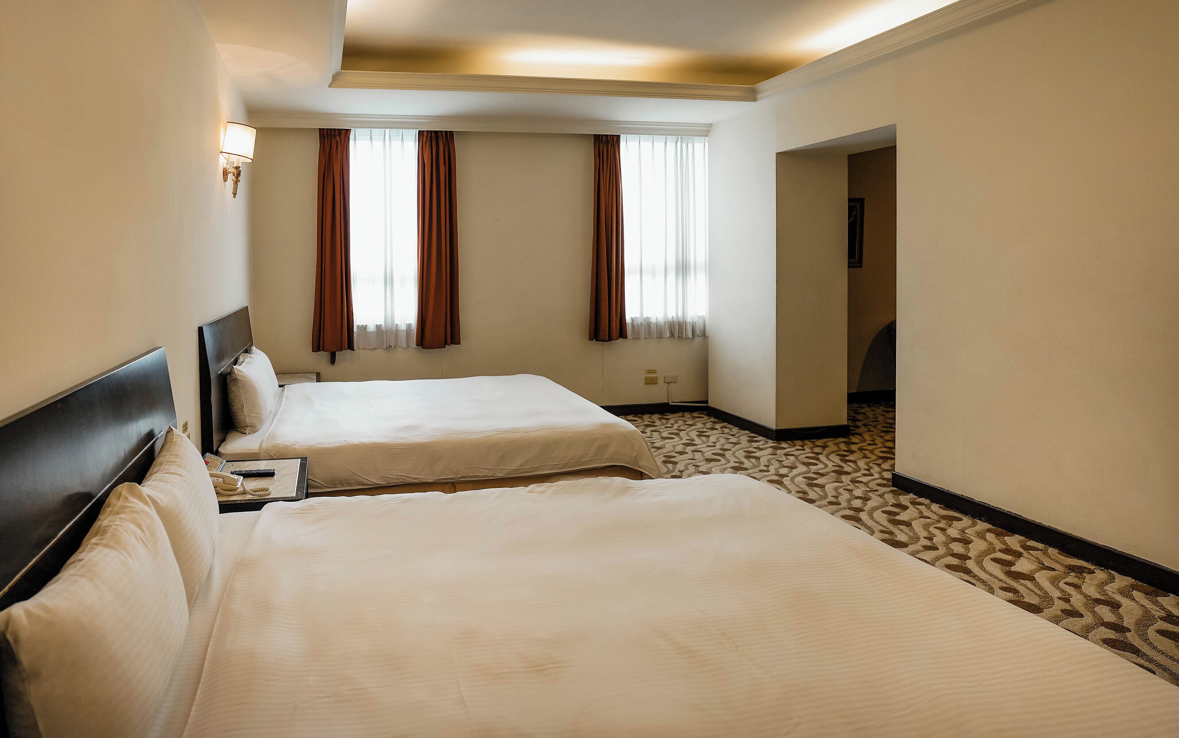 A hotel room with two beds, a carpeted floor, and a view of the hallway.