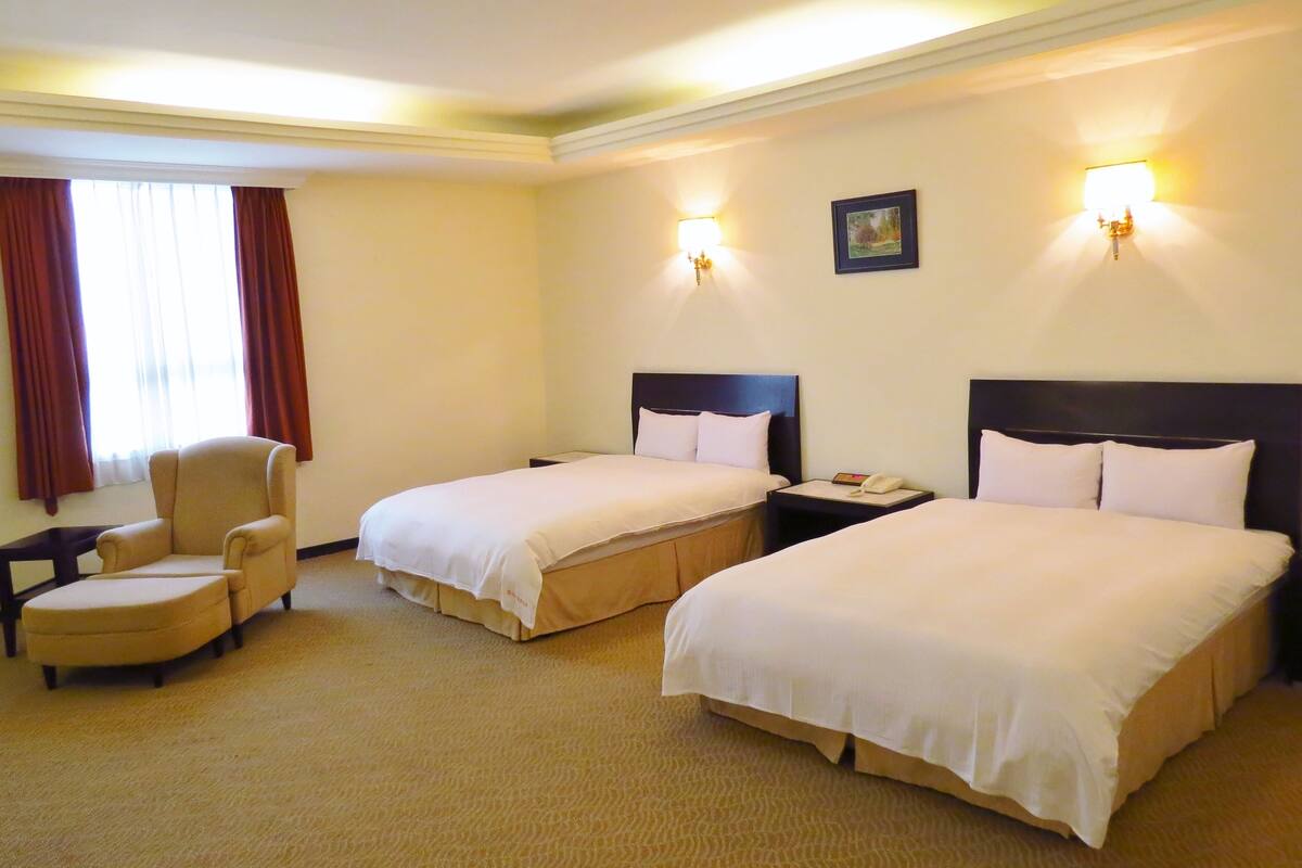 Camera d'albergo con due letti, una sedia, un comodino e una lampada.