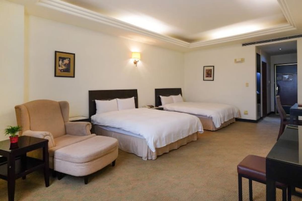 A hotel room with two beds, a chair, a small table, and a desk.