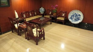 A traditional-style room with wooden furniture, including a sofa, chairs, and a table. There is a vase with flowers and a decorative plate on the wall. - Herkang Hotel (Taichung)