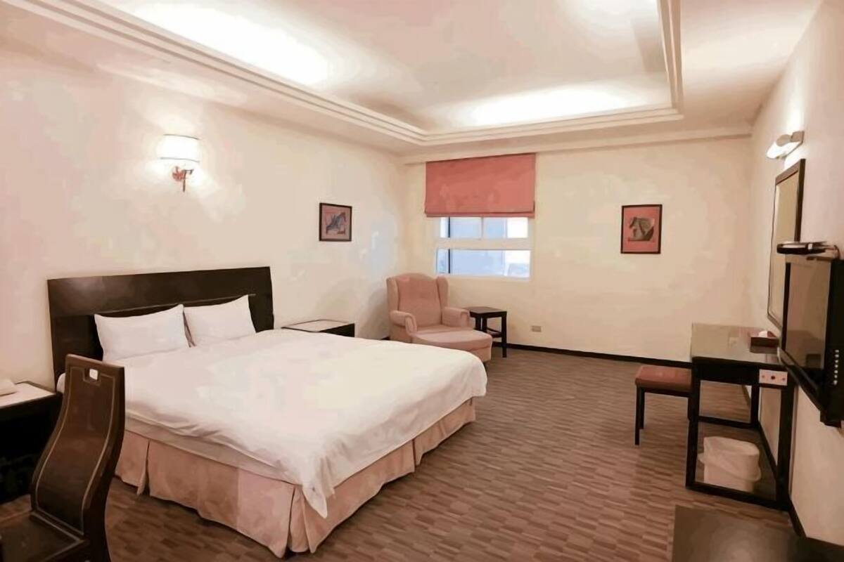 Una camera d'albergo con un letto grande, una scrivania, una sedia, un tavolino e una finestra con tenda.