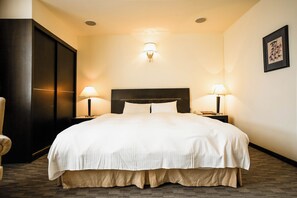 A hotel room with a large bed, two bedside lamps, a dark headboard, a wall-mounted light fixture, and a framed picture on the wall. - Herkang Hotel (Taichung)