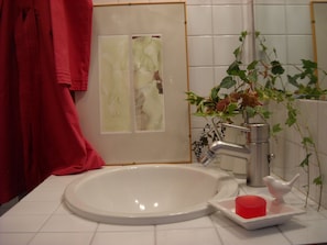 A bathroom with a white sink, a red towel, a plant, and a white bird-shaped soap holder. - La Casa del Giardiniere (Zero Branco)
