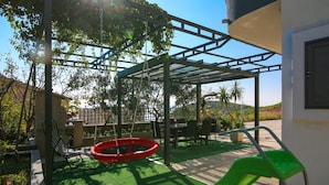 A covered outdoor area with a swing set, a red tire swing, and a green slide. - La Storia Apartments (Makarska)