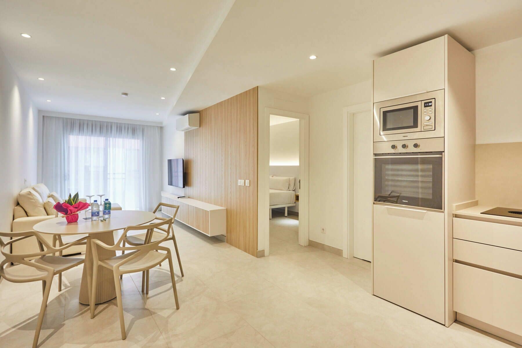 A modern hotel room with a dining area, kitchenette, and a bed.