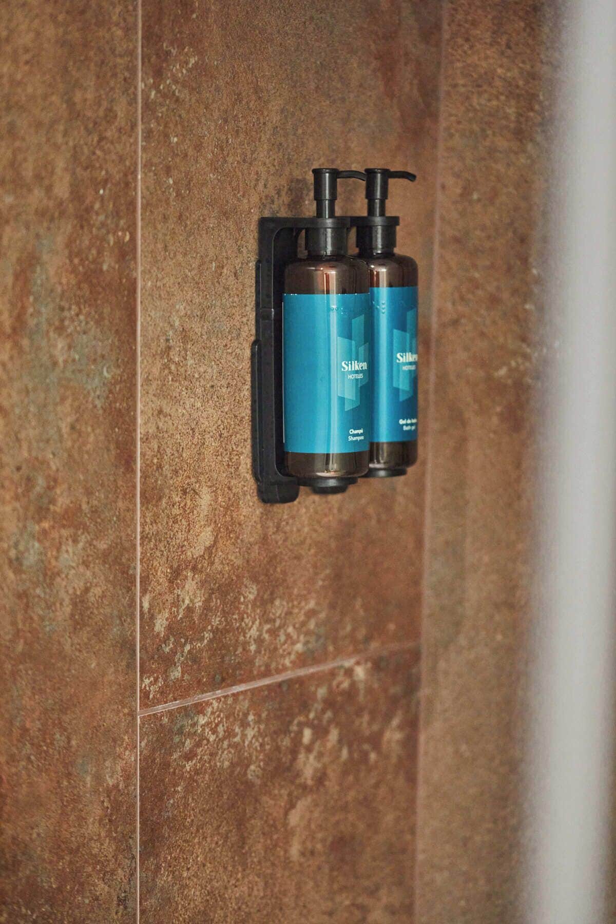 Ein Badezimmer mit Wandspender, der zwei Flaschen Silken-Hotelshampoo enthält.