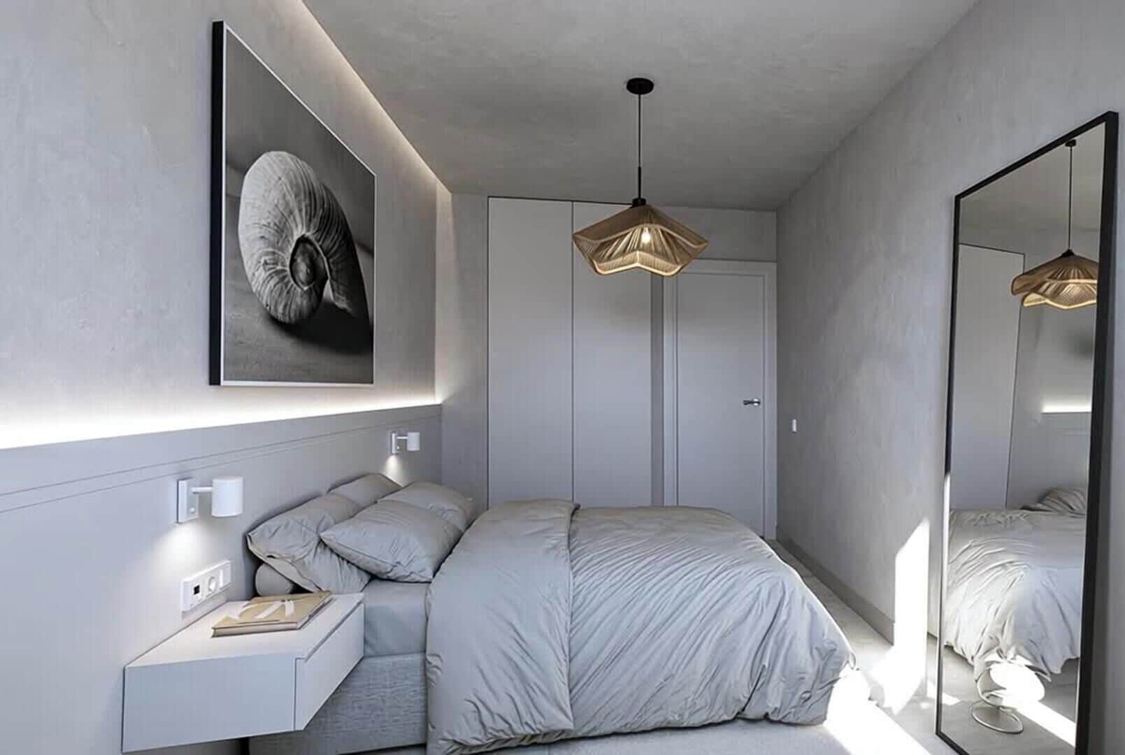 A modern bedroom with a bed, bedside table, wall-mounted light, and a large mirror.