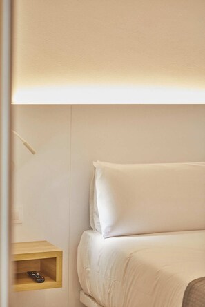 A bed with white bedding, a bedside table with a remote control, and a wall-mounted light fixture. - Silken Atlantis Playa – Holiday Homes (Las Palmas de Gran Canaria)