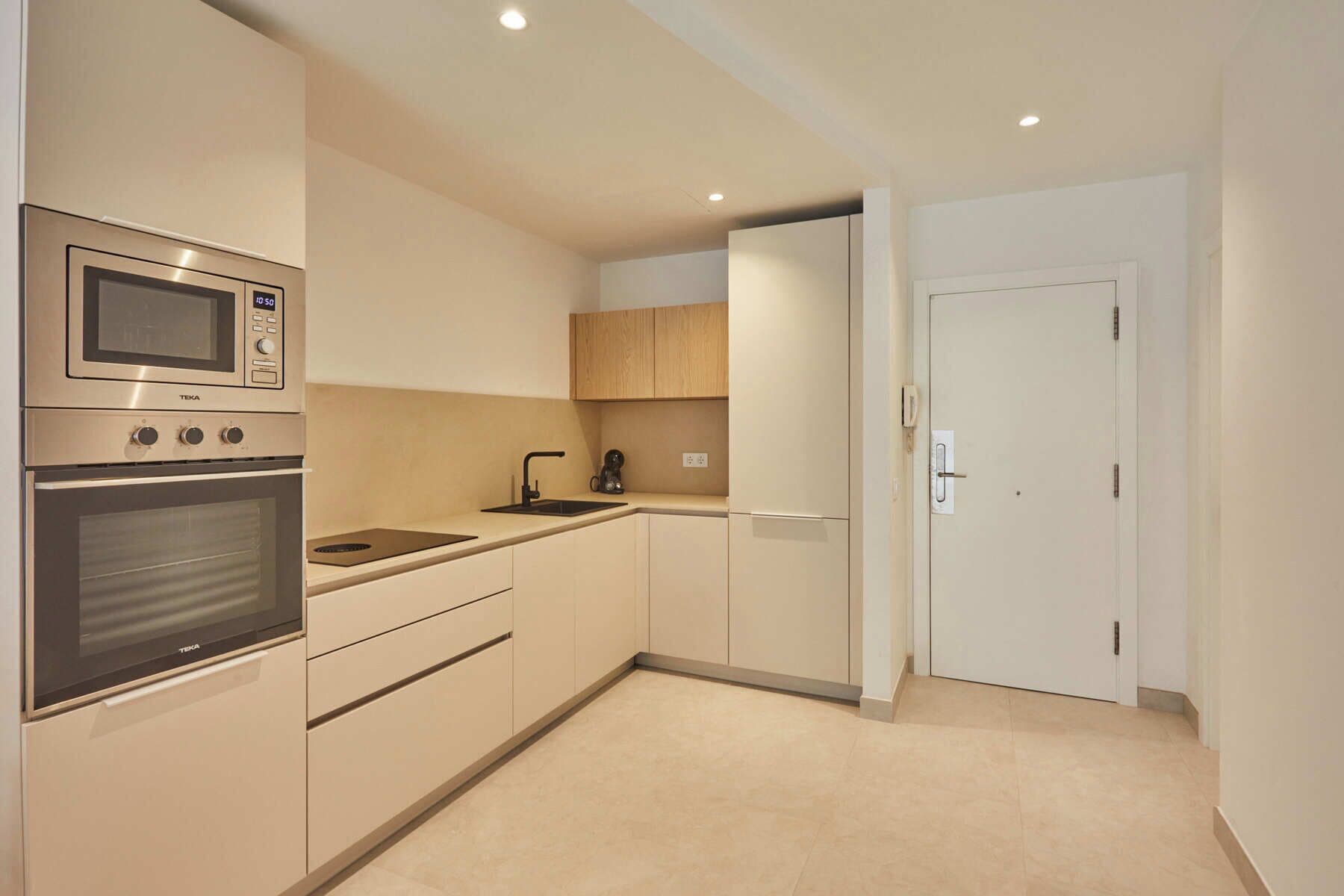 Una cocina moderna con electrodomésticos de acero inoxidable, armarios de madera y una puerta blanca.
