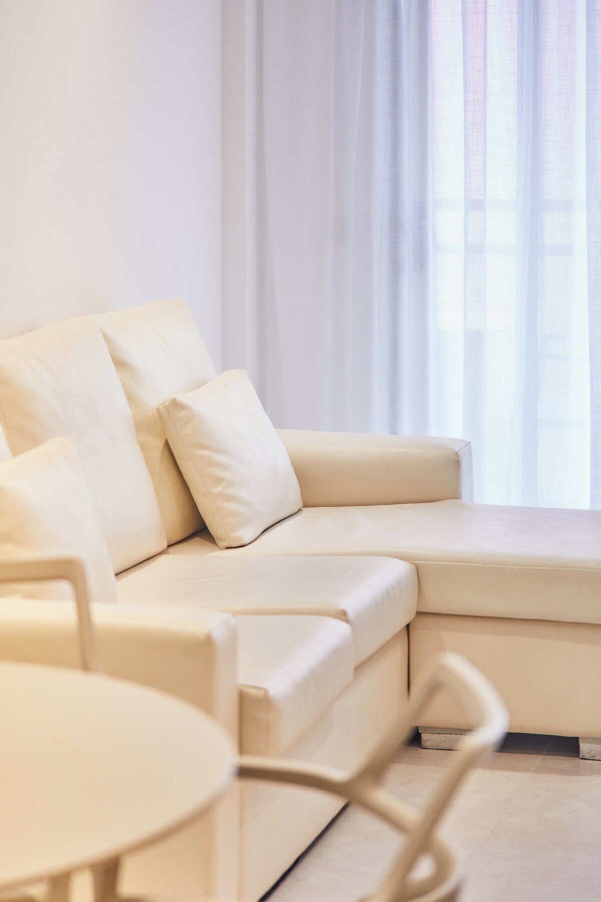 Un salon moderne avec un canapé d’angle beige, une table basse ronde et un coin repas avec une chaise.